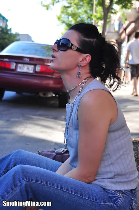 Brunette in Jeans and Glasses Smokes a Cigarette on a Busy Street – photo 1 of 15