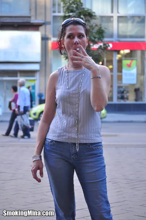 Brunette in Jeans and Glasses Smokes a Cigarette on a Busy Street – photo 14 of 15