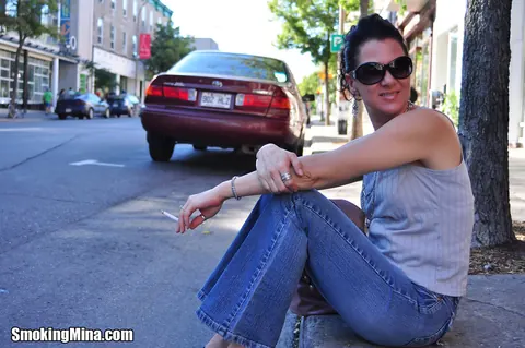 Brunette in Jeans and Glasses Smokes a Cigarette on a Busy Street – photo 3 of 15