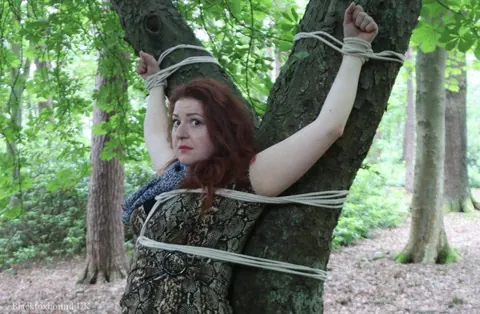 Redhead Bound to a Tree in a Forest Wearing a Skirt – photo 12 of 16