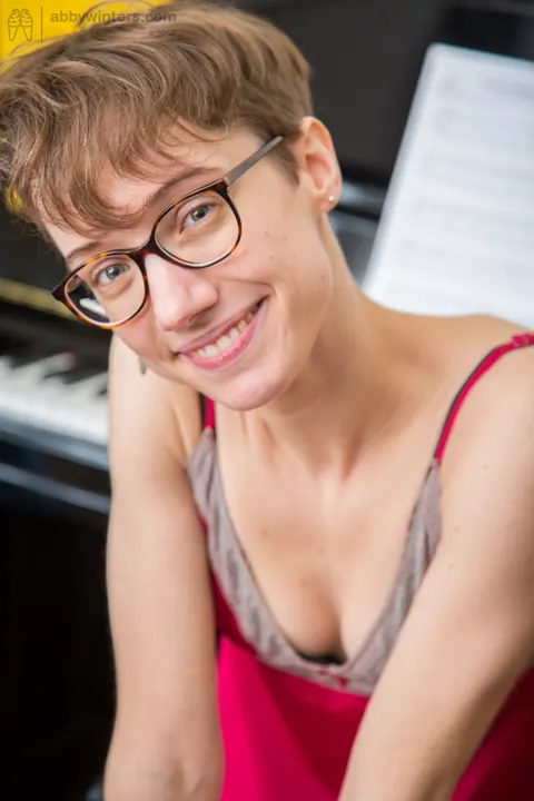 Slim Short-Haired Woman in Glasses Spreads on a Piano Bench – photo 1 of 16