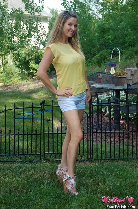 Kelly Anderson: Brunette MILF in Shorts and High Heels Shows Her Feet on Lush Grass – photo 1 of 15